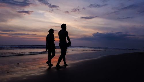 Silhouette friends walking at beach against sky during sunset