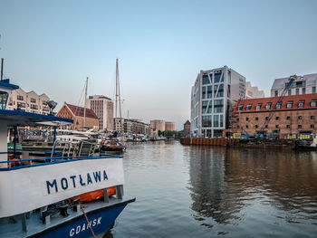 Sailboats moored on river by buildings in city against clear sky