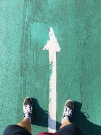 Low section of man standing over arrow sign on road