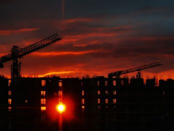 Silhouette cranes at construction site during sunset