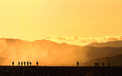 Silhouette people on landscape against sky during sunset