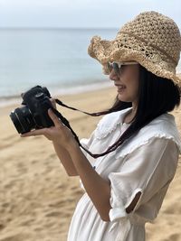 Midsection of woman holding camera at beach