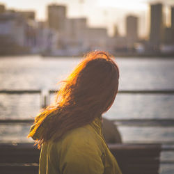 Rear view of female in yellow jacket watching genova city skyline on the sea at sunset