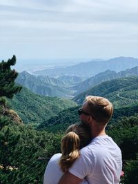 Rear view of couple embracing by mountains against sky