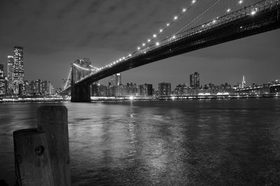 Illuminated bridge over river against sky in city at night