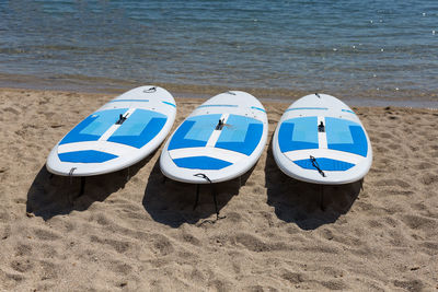 Three white surfboards resting on the shoreline on the beach.