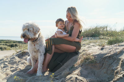 Full length of women sitting on shore with a child and dog