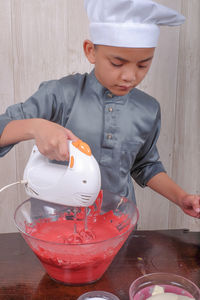 Boy mixing batter in bowl on table at home