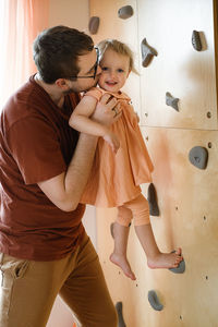 Father teaching toddler child to climb on wall, play active games. dad having fun with kids at home