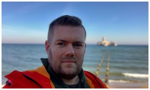 Portrait of bearded man standing against sea 