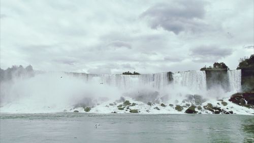Waves splashing on rocks against cloudy sky