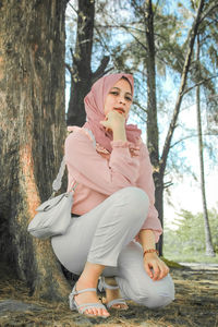 Young woman using mobile phone while sitting on tree