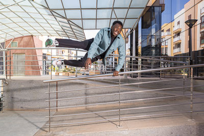 Positive african american guy smiling and jumping over railing on street
