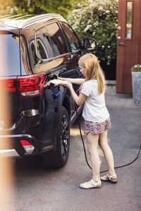 Blond girl charging black electric car in back yard