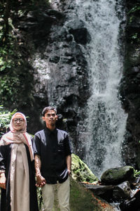 Couple looking away while standing against waterfall