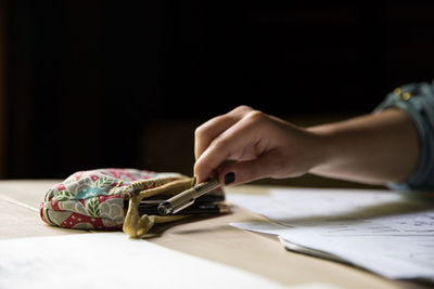 Cropped image of woman holding pen by pencil case at table