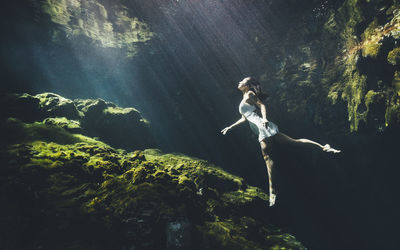 Woman underwater by rock formation 