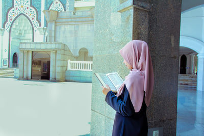 Side view of woman holding umbrella against buildings