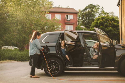 Girls looking at smiling mother charging electric car at station