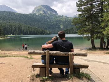 Rear view of man sitting on seat in lake against mountains