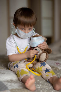 A little boy in a mask sitting on the bed and stetoscope a teddy bear. image with selective focus