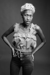 Portrait of young woman standing against gray background