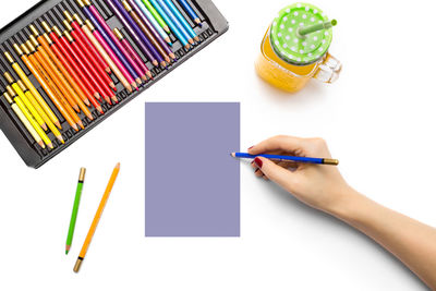 Midsection of person holding colored pencils against white background