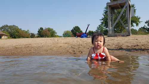 Portrait of cute girl sitting in sea against sky