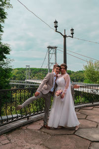 Couple holding umbrella while sitting on bridge