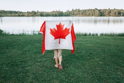 Rear view of girl holding canadian flag against lake