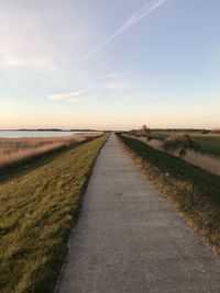 Empty road amidst field against sky during sunset