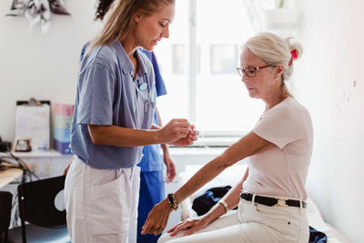 Doctor applying bandage on hand of senior woman in medical examination room