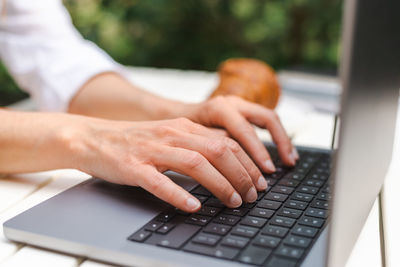 Unrecognizable female hands are typing on a laptop keyboard during a business meeting in a cafe.