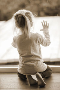 Rear view of girl kneeling by window