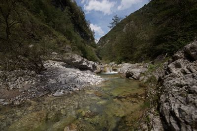 Stream flowing through rocks by river against sky