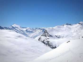 Low angle view of snowcapped mountains against clear blue sky