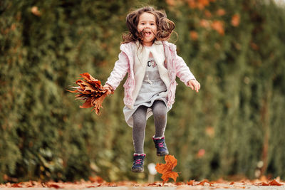 Full length of girl holding leaves jumping at park