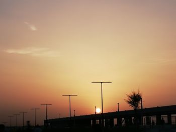 Street lights and silhouette bridge against sky during sunset