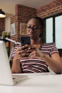 Young woman using mobile phone while sitting at home