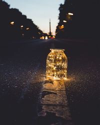 Illuminated glass jar on road at dusk