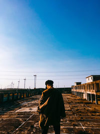 Rear view of man standing on railroad track against sky