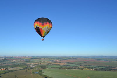 Hot air balloon flying over landscape against clear blue sky