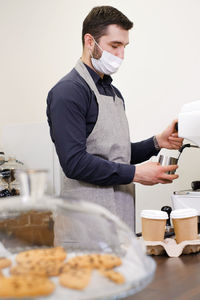 Barista serving coffee in takeaway cups in coffee shop in protective mask. coffee to go during