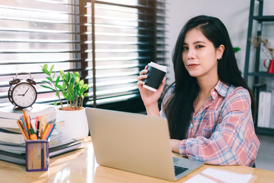 Young woman using phone while sitting on table