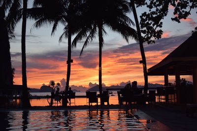 Silhouette palm trees by swimming pool against sky during sunset