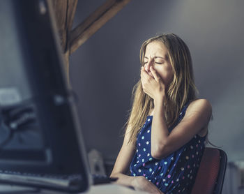 Girl yawning while sitting by computer at table