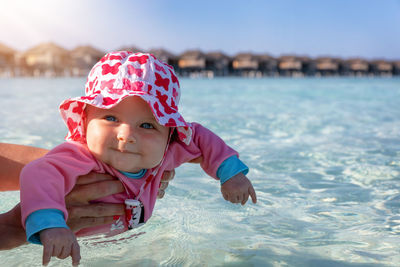 Cropped hands holding smiling baby girl on sea