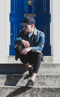 Fashionable man sitting on steps against blue door
