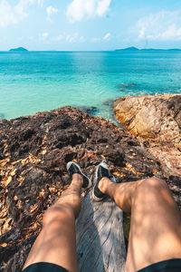 Low section of feet on rock in sea against sky