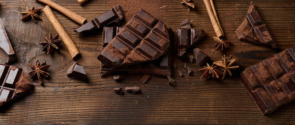 Broken pieces of dark chocolate, cinnamon sticks and star anise on a brown wooden table, top view